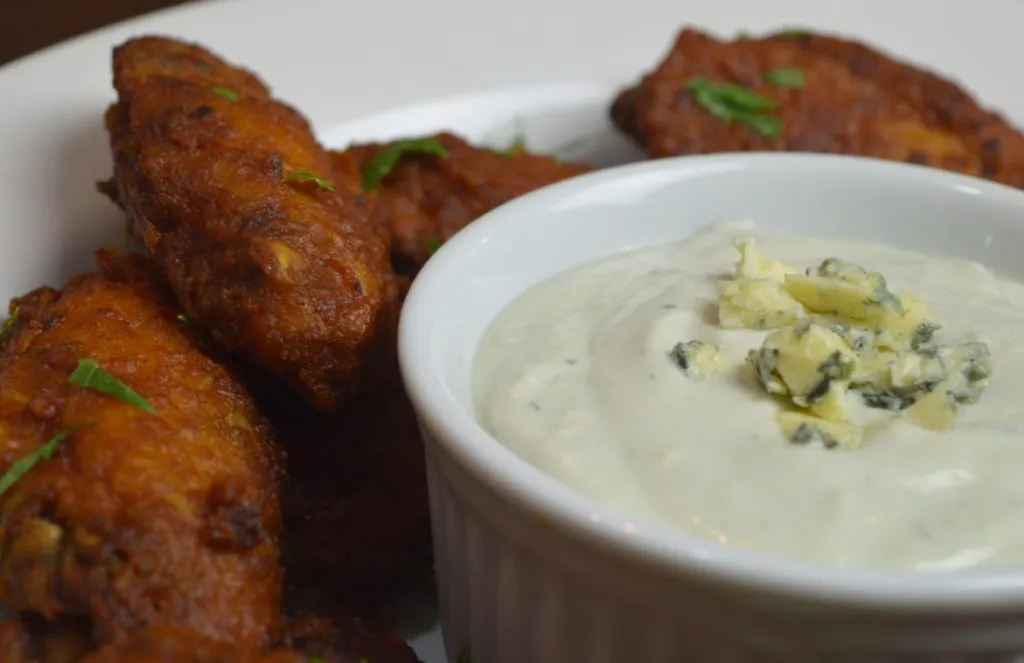 Asas de frango fritas com salsinha ao lado de molho cremoso de queijo azul em ramequim