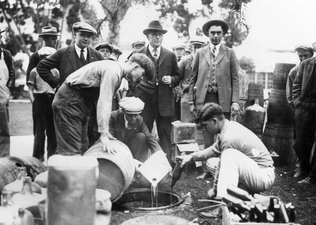 Homens de época despejando cerveja de barris e garrafas em um bueiro, durante a Lei Seca americana
