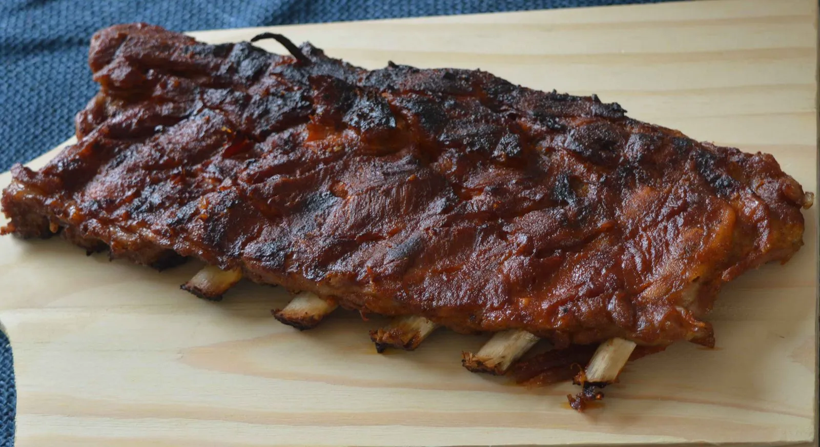 Costelinha com barbecue pronta, com crosta escura caramelizada, sobre tábua de madeira