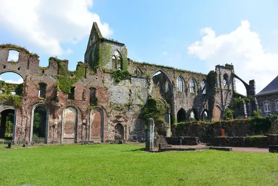 Ruínas de arcos góticos da Abbaye d'Aulne, com paredes de pedra cobertas de vegetação e gramado à frente