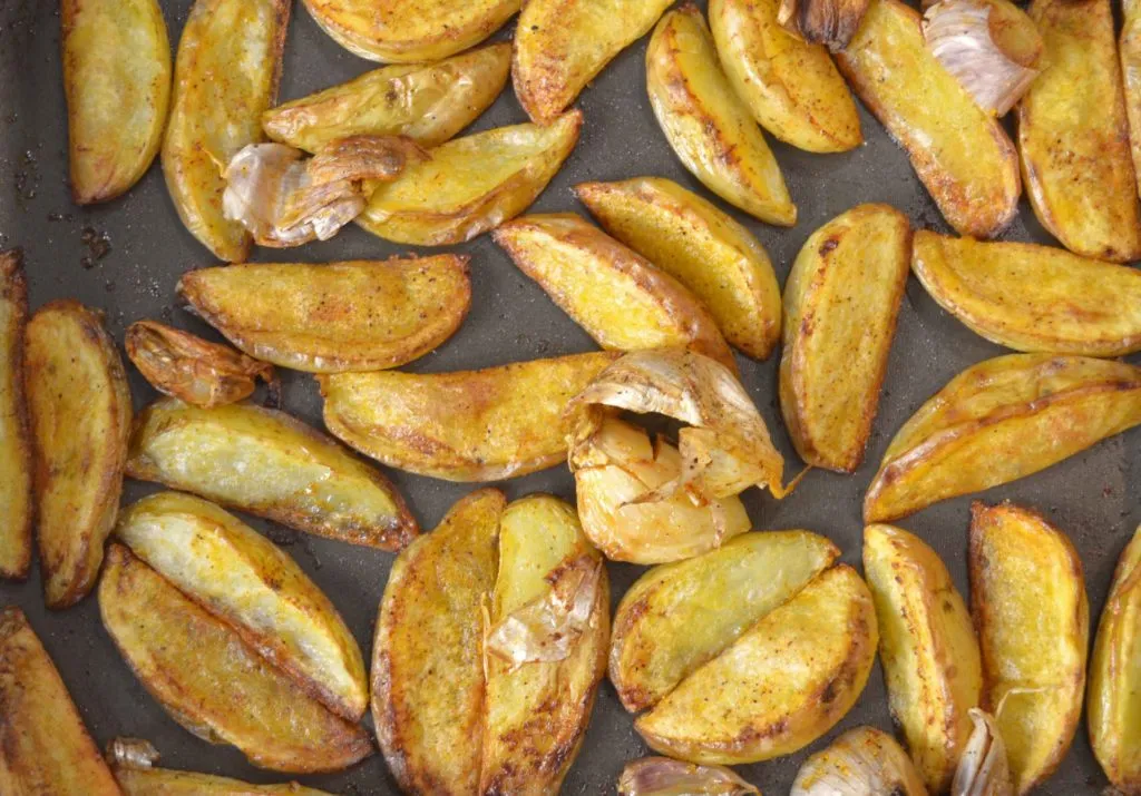 Batatas rústicas assadas, douradas, com dentes de alho, em assadeira escura