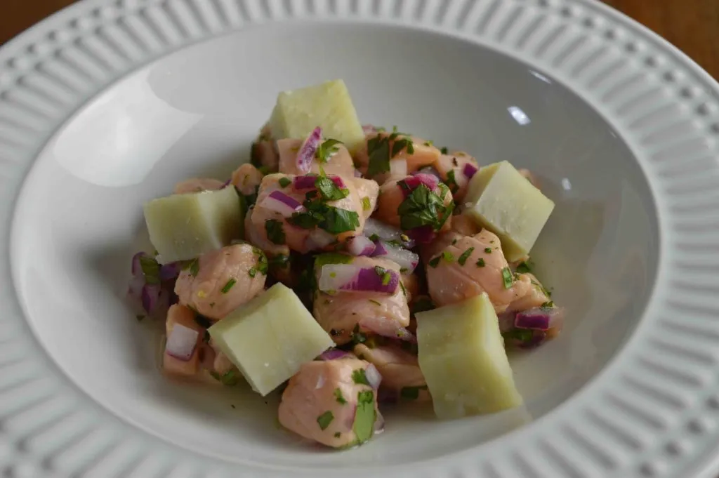Ceviche de salmão com cebola roxa, coentro e cubos de mandioca em prato fundo branco