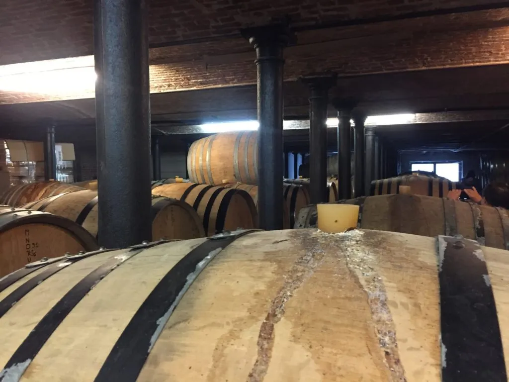 Sala de maturação com barris de carvalho e colunas de ferro sob teto de tijolos, na Cantillon