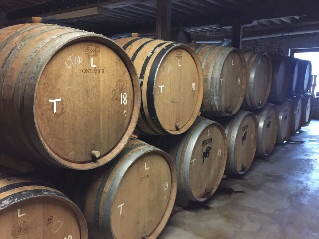 Barris de carvalho empilhados na adega da Cantillon, marcados com letras e números a giz
