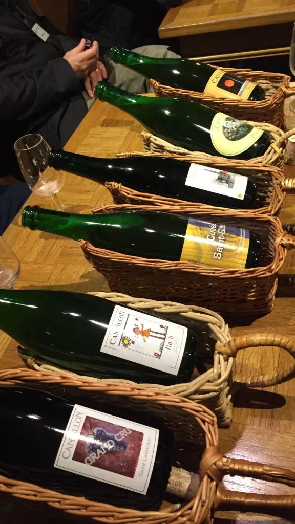 Garrafas de Cantillon deitadas em cestos de vime sobre a mesa, entre elas Cuvée Saint-Gilloise e Grand Cru
