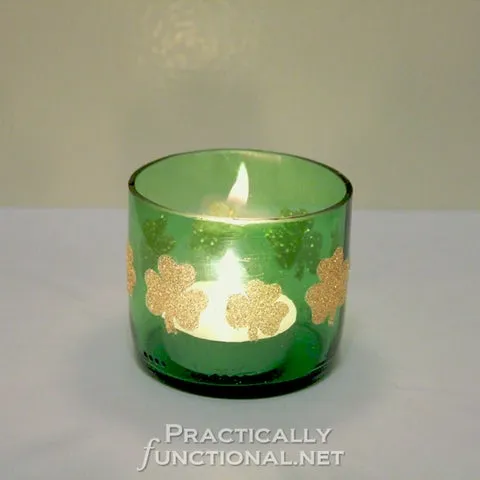 Vela acesa dentro de uma garrafa verde cortada, decorada com trevos dourados