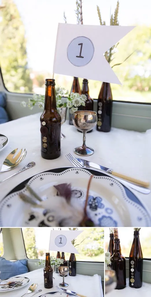 Garrafas de cerveja com botões colados e flores na mesa, com plaquinha numerada 1 identificando a mesa