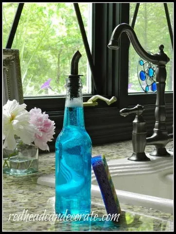 Garrafa de cerveja com detergente azul e bico dosador ao lado da pia, usada como saboneteira líquida