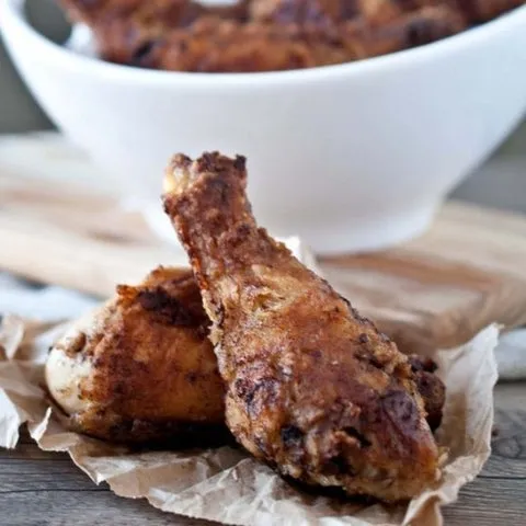 Coxas de frango empanadas e fritas sobre papel, com tigela branca ao fundo