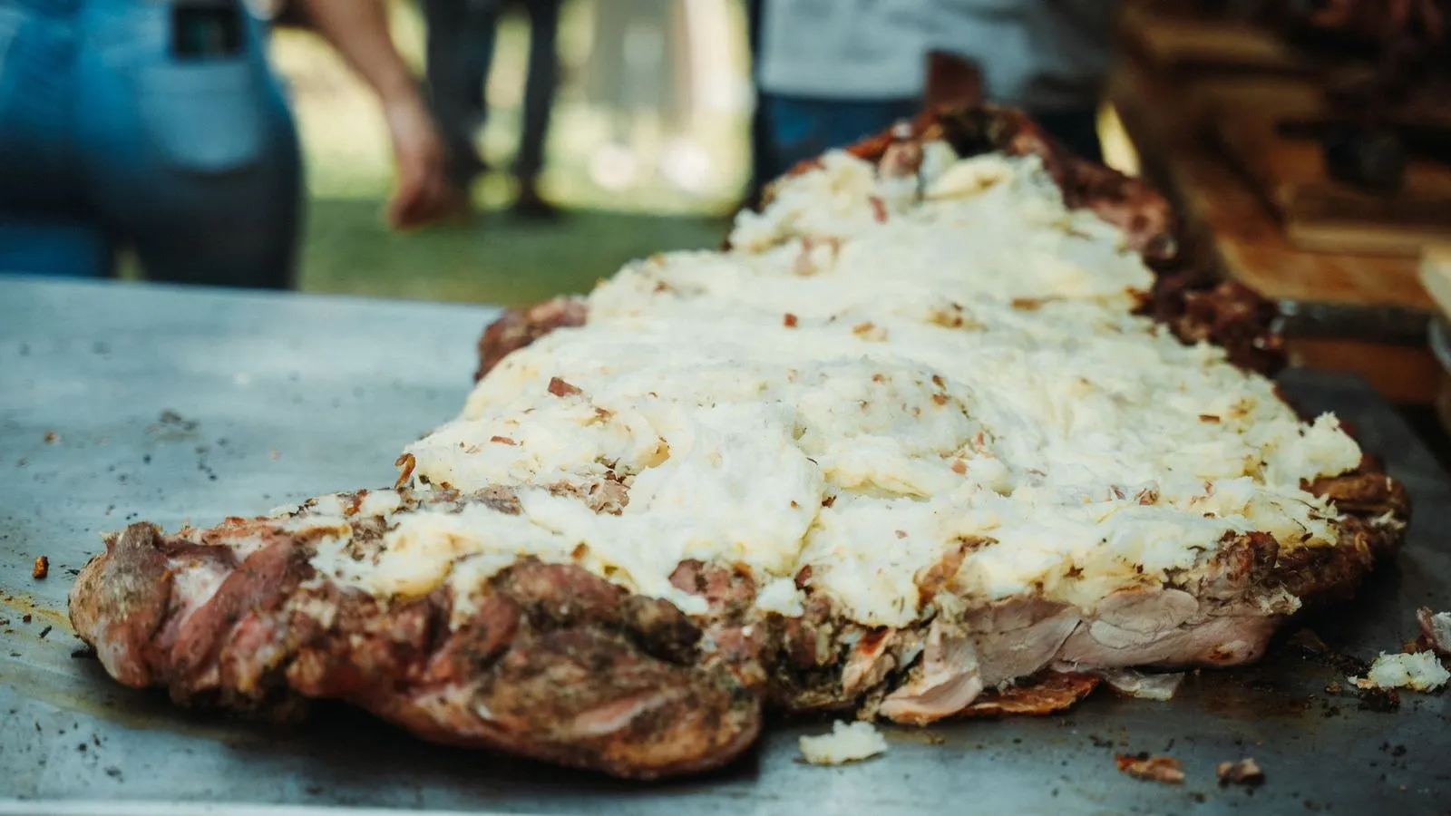 Peça grande de carne assada coberta por purê cremoso sobre uma mesa de metal