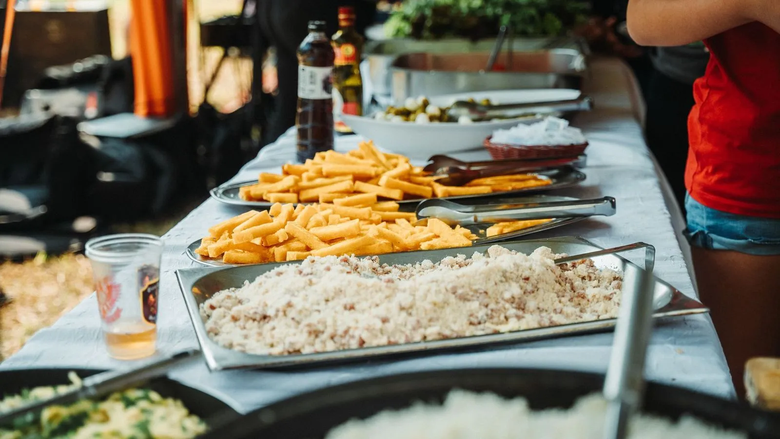 Bufê do evento com travessas de polenta frita, farofa e outros acompanhamentos, e copo de cerveja ao lado