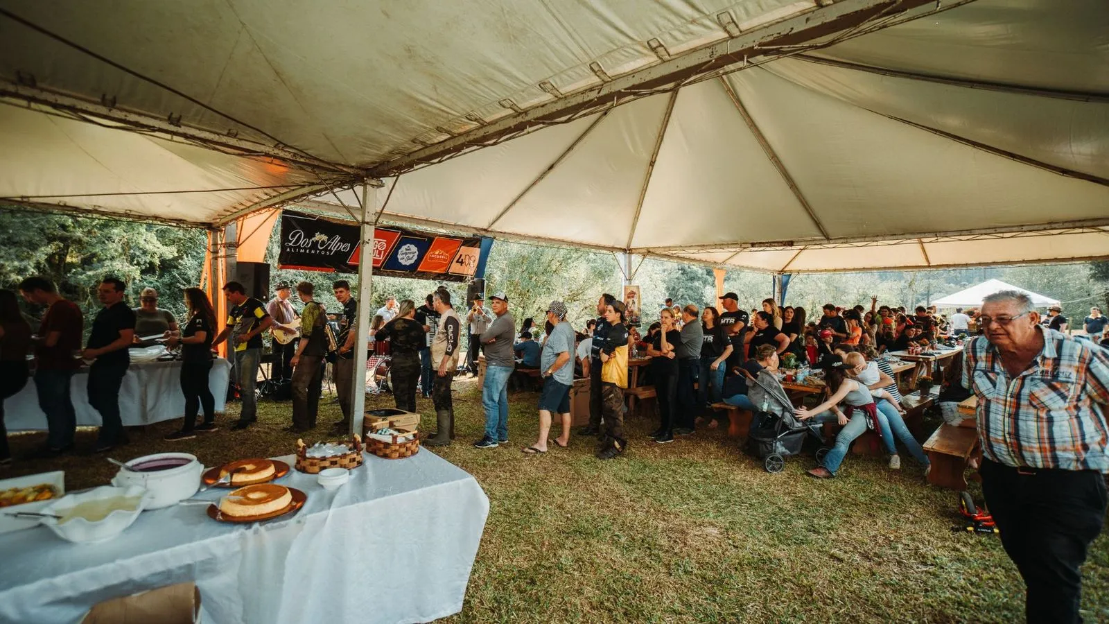 Grande tenda com fila no bufê e mesas cheias de participantes do Quadrifest, com música ao fundo