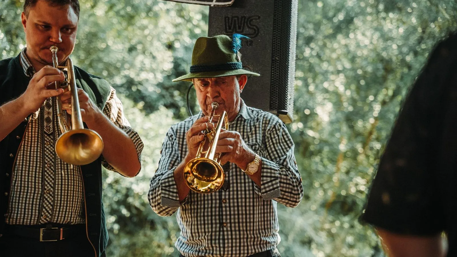 Dois músicos tocando trompete, um deles de chapéu tirolês com pena azul