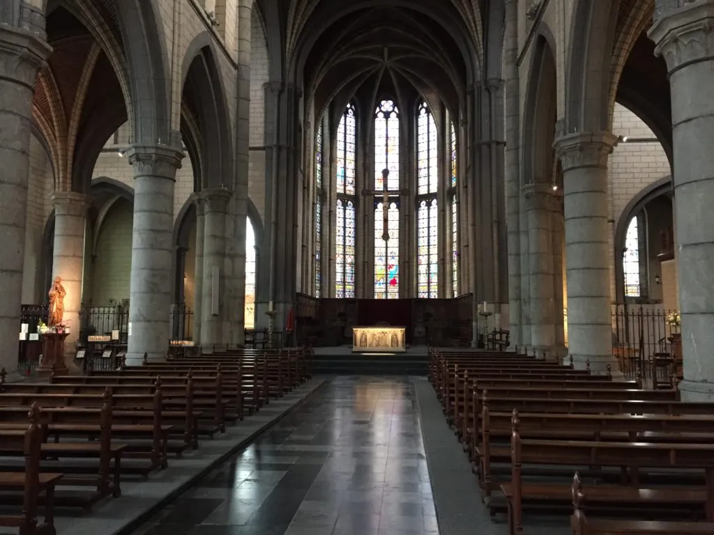 Interior da igreja da Abadia Val-Dieu, com colunas de pedra, bancos de madeira e vitrais ao fundo