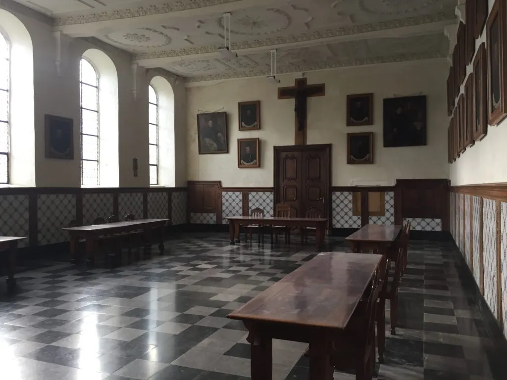 Sala de refeições dos monges da Abadia Val-Dieu, com mesas de madeira, retratos nas paredes e crucifixo