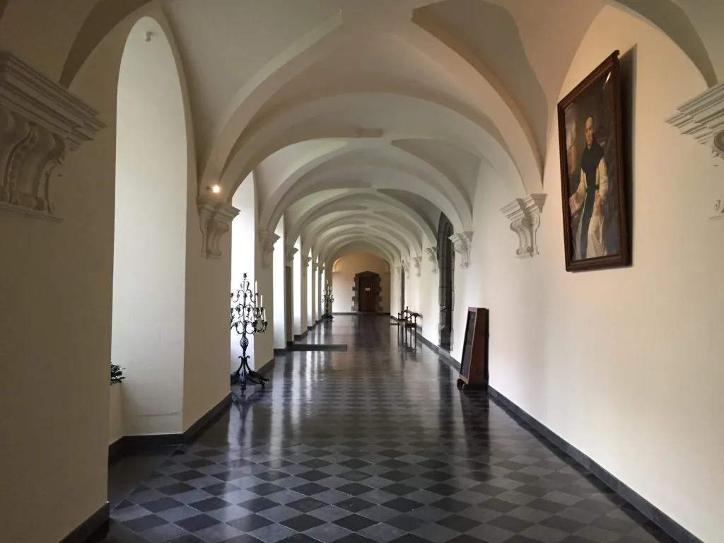 Galeria com teto em arcos e piso xadrez na Abadia Val-Dieu, com um retrato de monge na parede