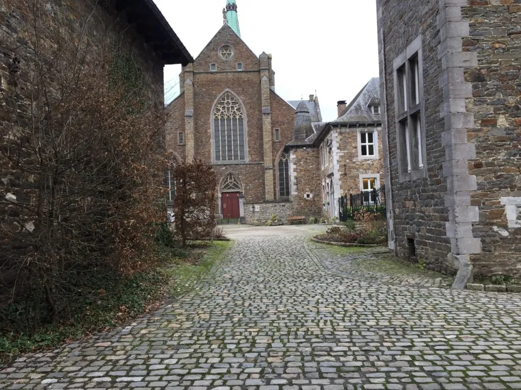 Pátio de paralelepípedos da Abadia Val-Dieu, com a igreja de tijolos e janela gótica ao fundo