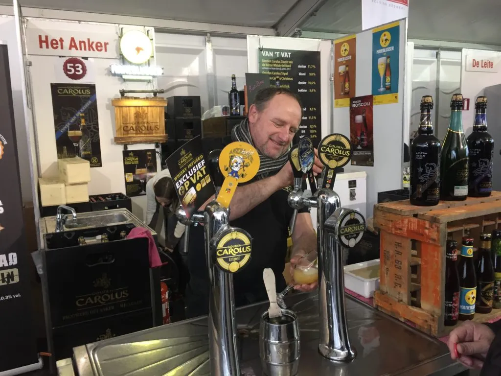 Homem tira chope em estande da Het Anker com torneiras Gouden Carolus e garrafas expostas no balcão