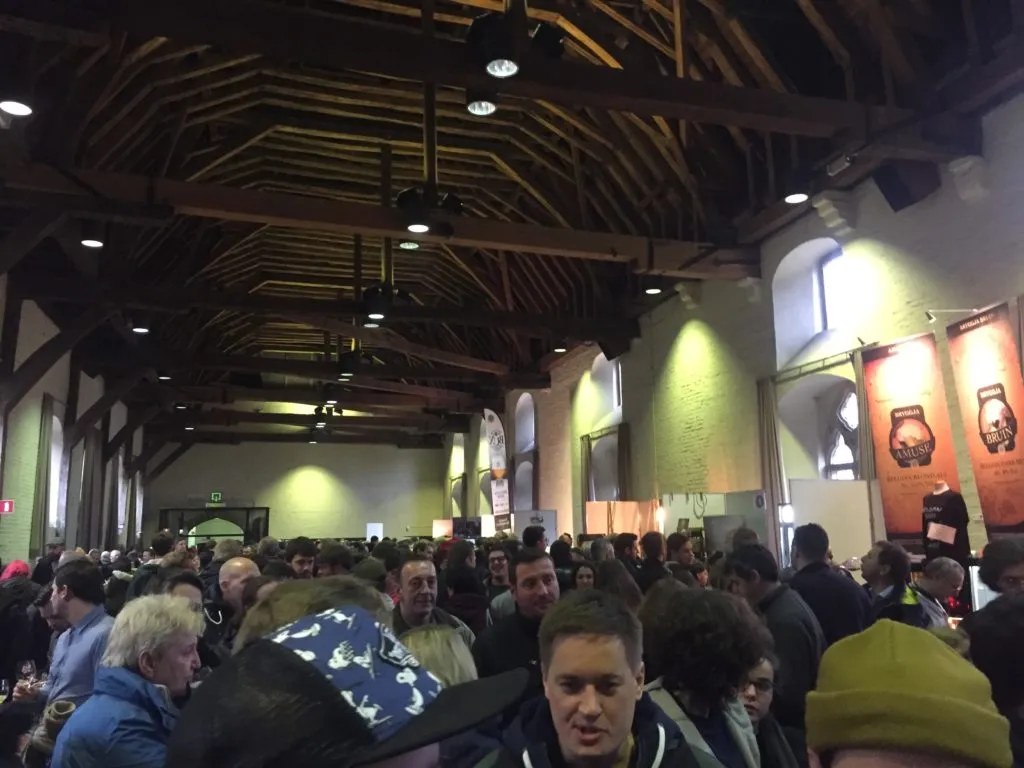 Salão com teto de vigas de madeira lotado de visitantes durante o Brugs Bierfestival