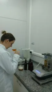 Analista de laboratório de jaleco examinando amostra de cerveja ao lado de equipamentos de medição