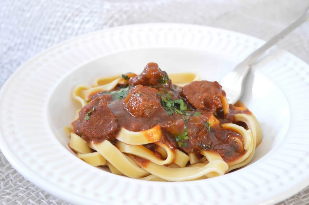 Prato de fettuccine com pedaços de carne de goulash ao molho, salsinha e garfo