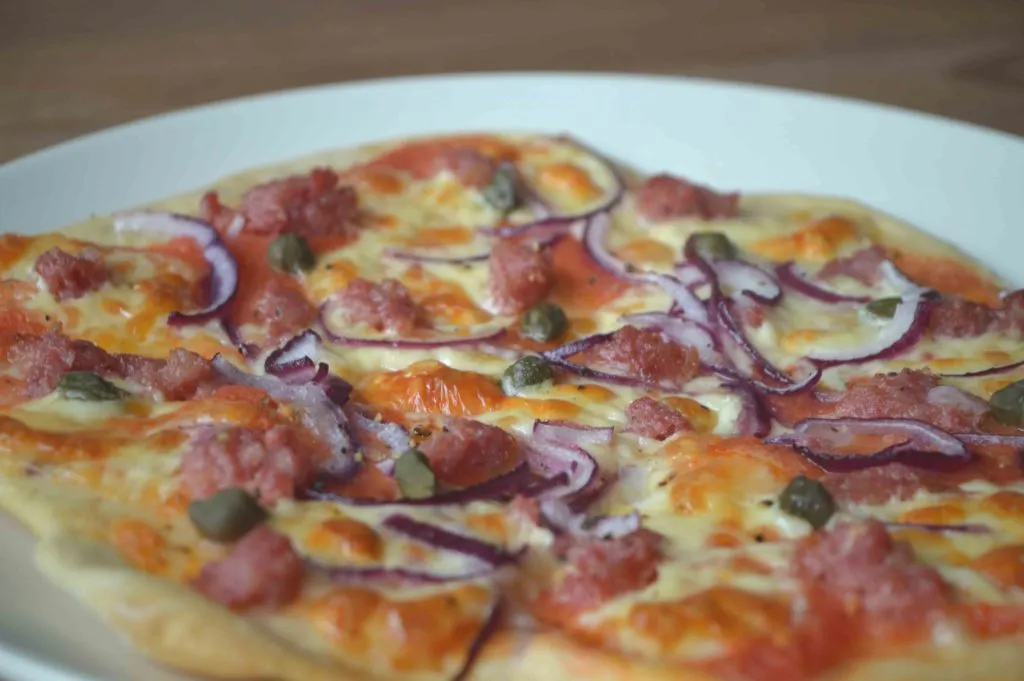 Cerveja sendo servida de garrafa Alt Bier Bierbaum em copo, ao lado de prato com pizza caprese