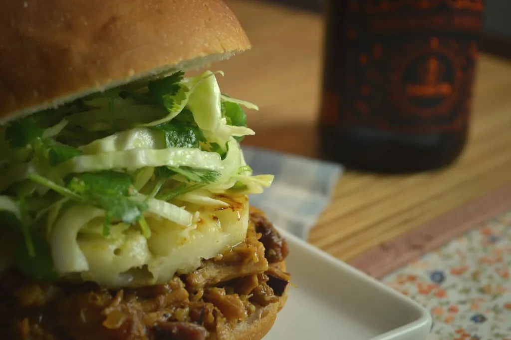 Sanduíche de pernil desfiado com queijo grelhado e salada de repolho e coentro, com garrafa ao fundo