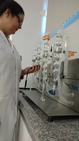 Pessoa de jaleco branco opera equipamento de laboratório com tubos de vidro, análise de cerveja do LATEB