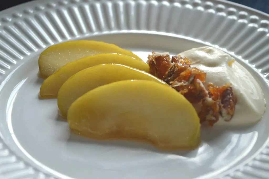 Sobremesa com fatias de maçã caramelizadas, creme e crocante de nozes em prato branco
