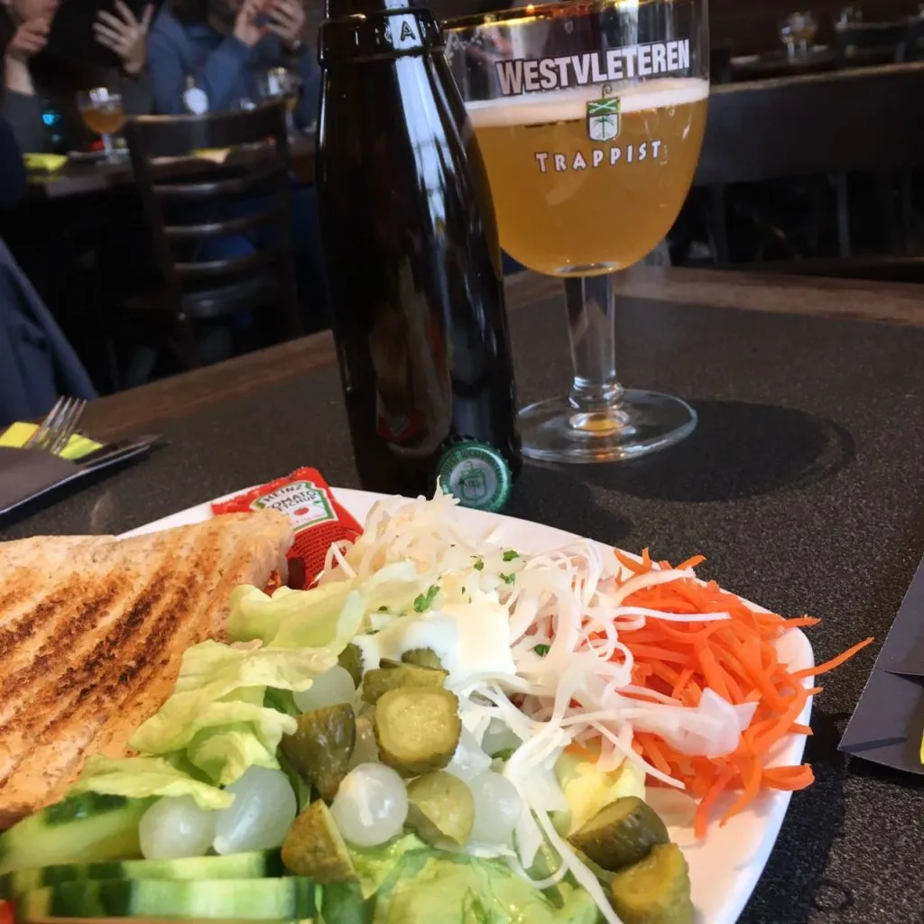 Sanduíche tostado e salada ao lado de garrafa e taça de cerveja dourada Westvleteren Trappist