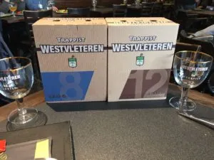 Caixas de cerveja Westvleteren 8 e 12 sobre mesa, entre duas taças