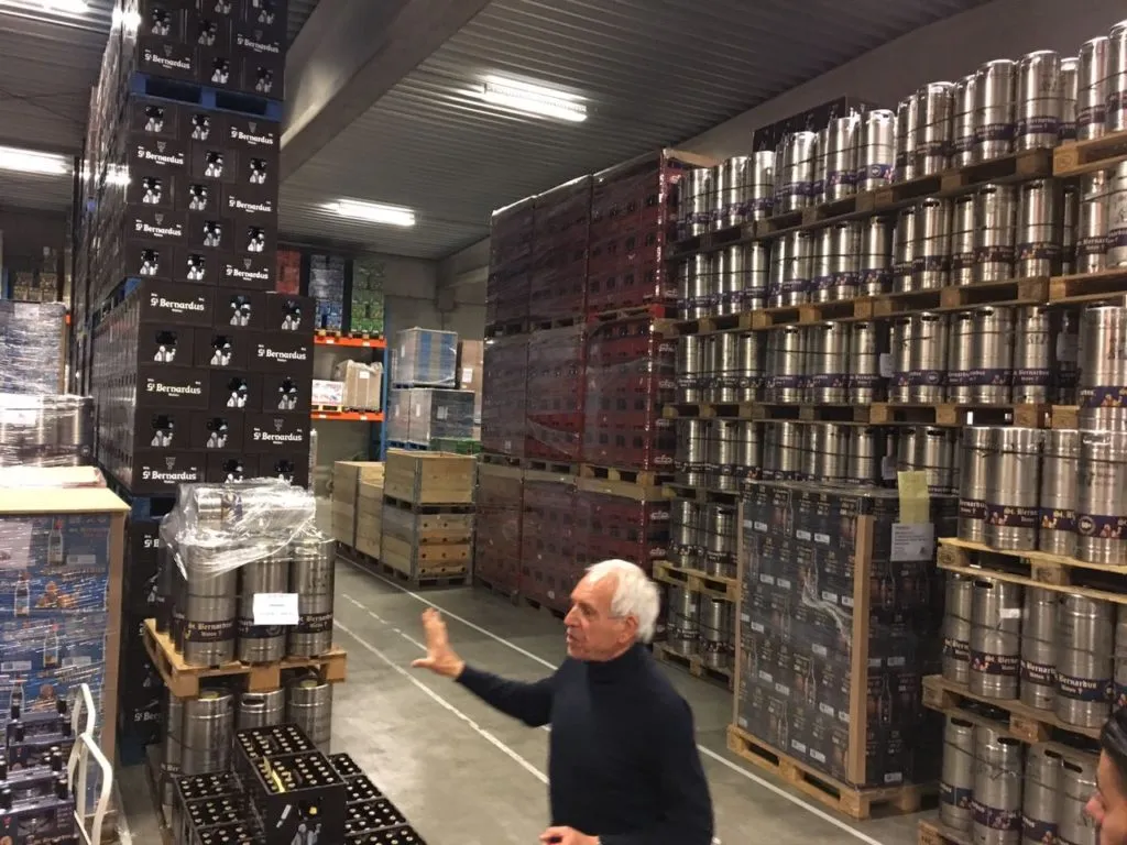 Depósito da St. Bernardus com caixas e barris de aço empilhados e um homem gesticulando