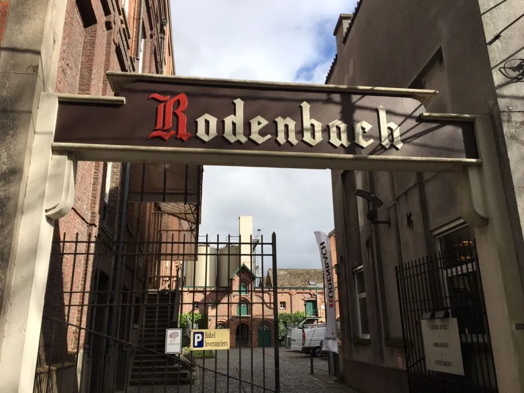 Portal da cervejaria Rodenbach, com letreiro e prédios de tijolo ao fundo, na Bélgica