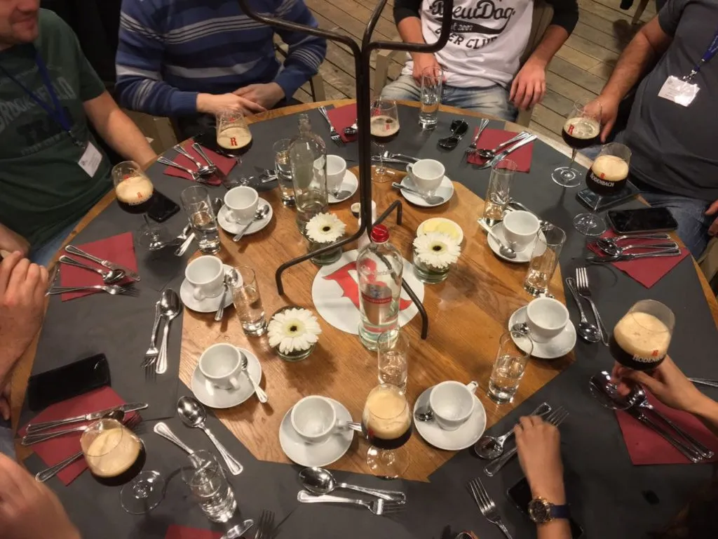 Mesa redonda com taças de cerveja escura Rodenbach, xícaras de café, copos e flores, vista de cima