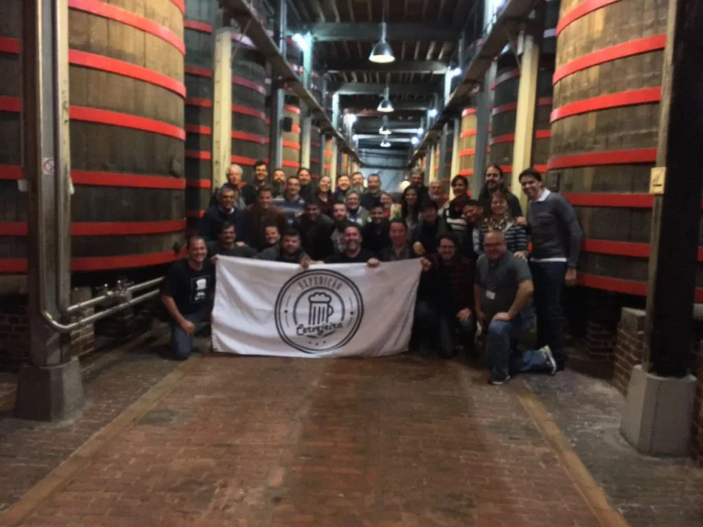 Grupo da Expedição Cervejeira posando com a bandeira entre as dornas de madeira da Rodenbach