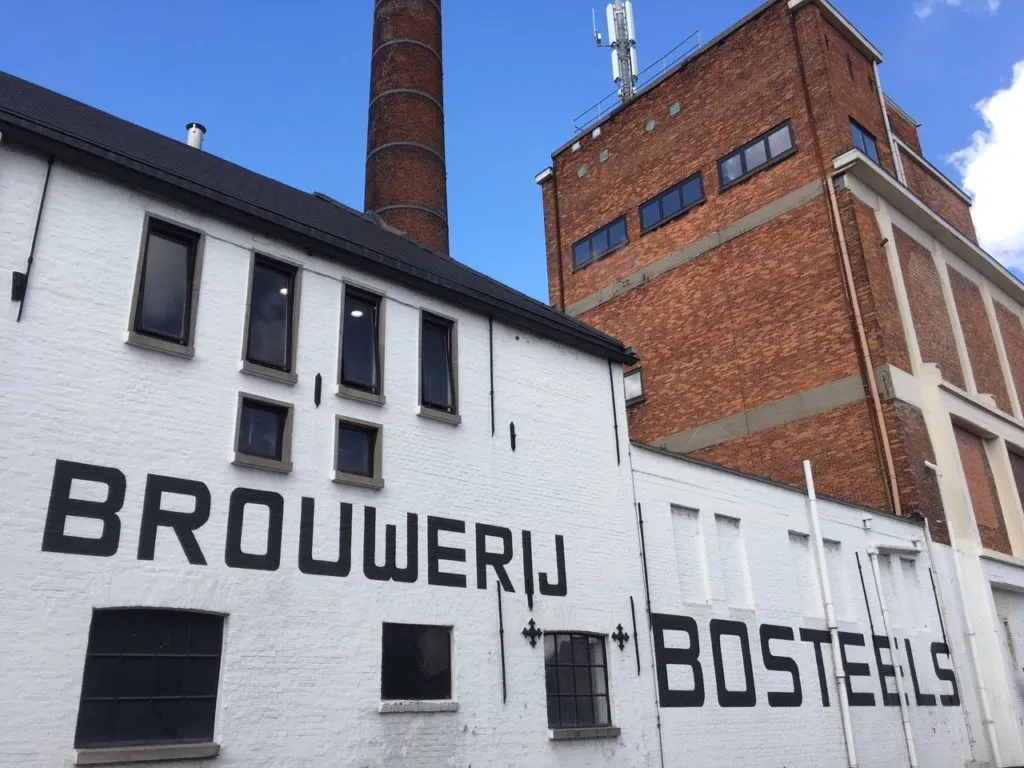 Fachada da cervejaria Bosteels, com a inscrição Brouwerij Bosteels e chaminé de tijolo