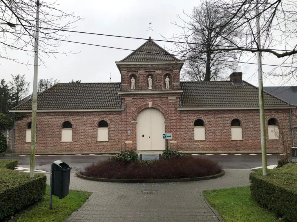 Fachada de tijolos da Abadia de Saint Sixtus, com três estátuas na torre, em dia nublado
