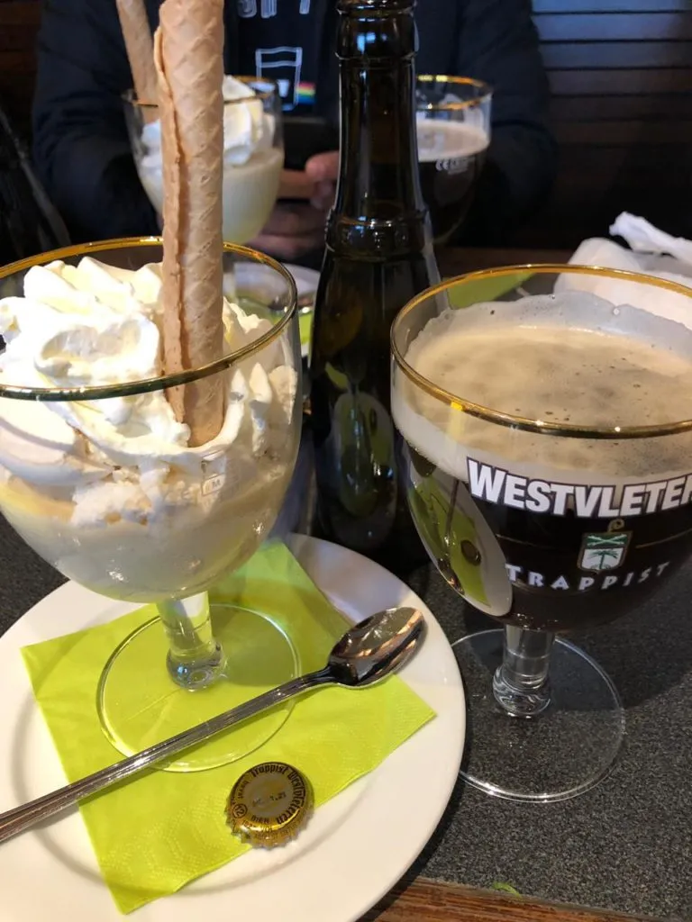 Sobremesa com chantilly e canudo de biscoito, taça de cerveja Westvleteren e garrafa sobre a mesa